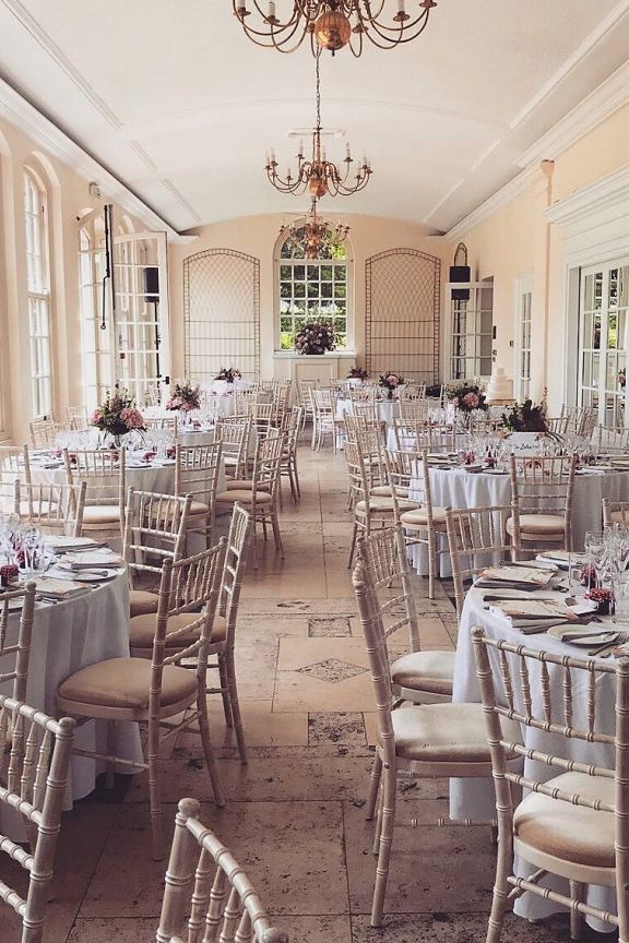 The Orangery function room setup with several round banqueting tables and chandeliers hanging from high ceilings. 